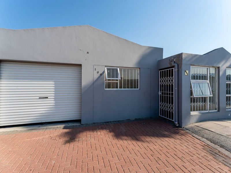 Front elevation of the property featuring a roller garage door, paved driveway, and secure entrance with security gate and window bars.