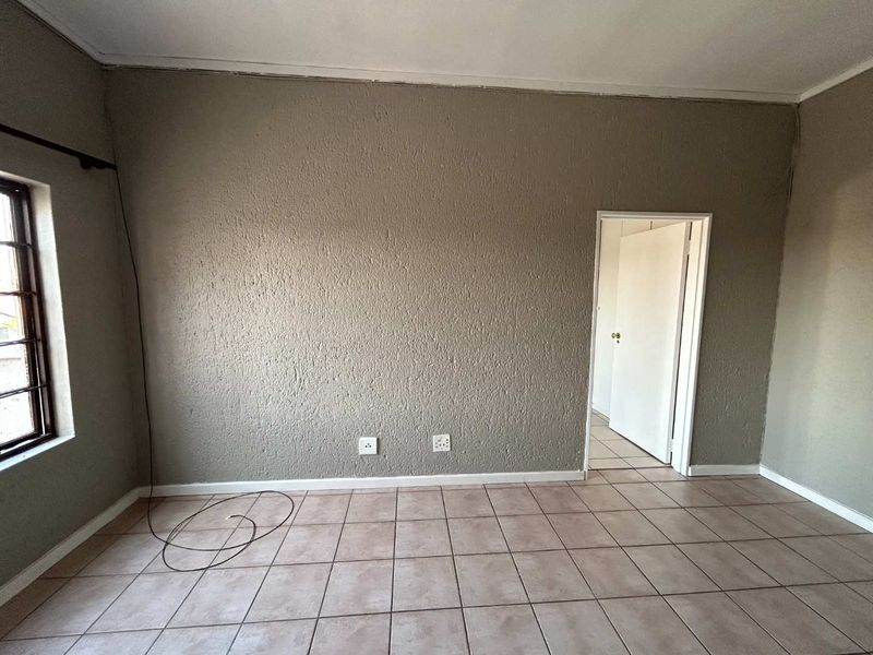 An empty living area featuring neutral tiled flooring, textured walls, and a window with security bars, offering a blank canvas for interior design.