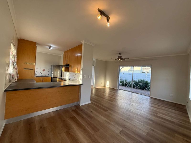 Open-plan living and kitchen area featuring wood-look laminate flooring, built-in cabinetry, and a sliding glass door leading to the outdoor patio.