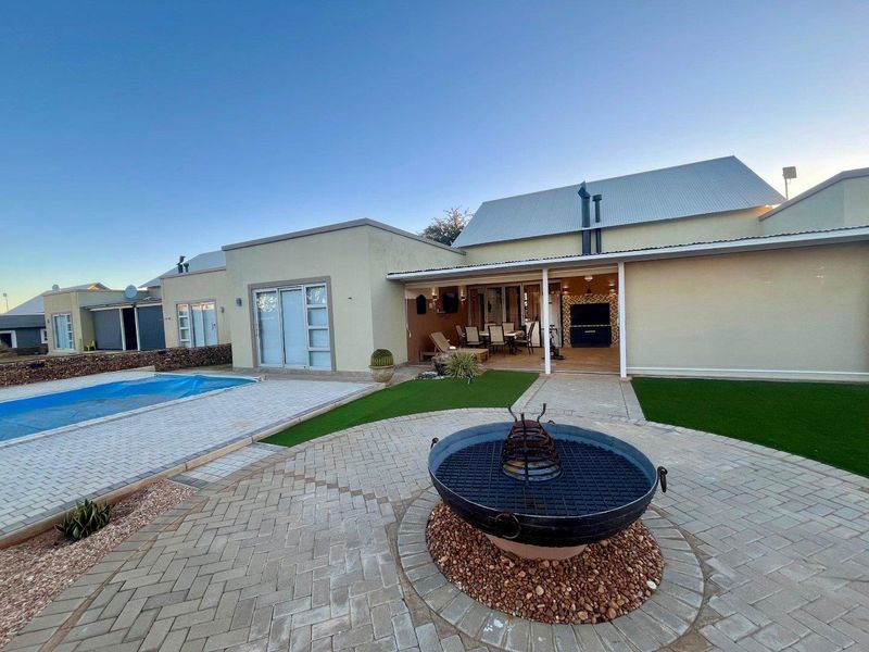 Rear exterior view featuring a swimming pool, paved patio area with a built-in braai, and well-maintained artificial lawn.