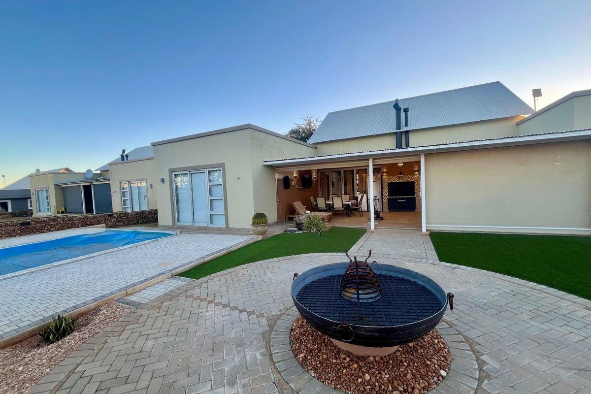 Rear exterior view featuring a swimming pool, paved patio area with a built-in braai, and well-maintained artificial lawn.