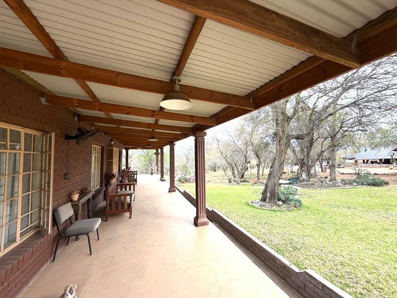 A spacious covered patio featuring exposed timber beams, brick columns, and direct access to the garden, offering a functional outdoor living space.