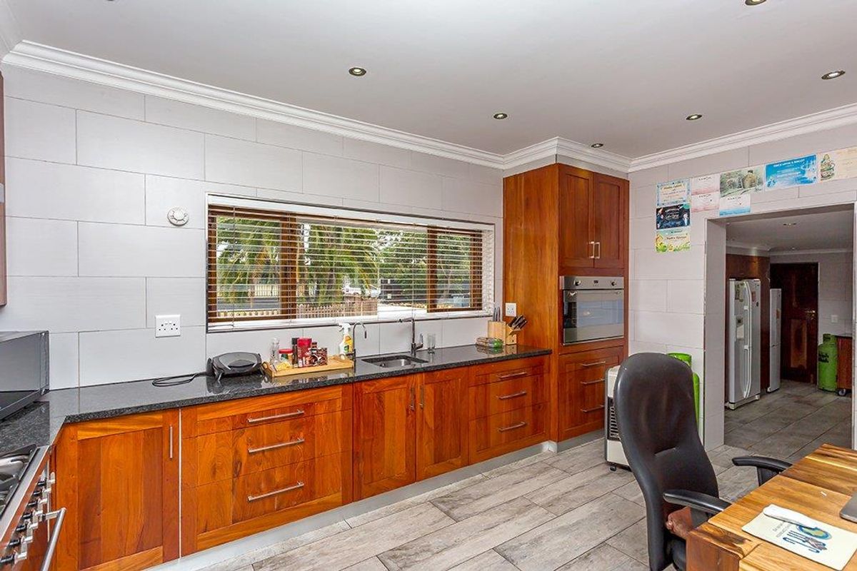 A well-maintained kitchen featuring warm wooden cabinetry, granite countertops, a built-in oven, and modern tiled finishes with ample natural light.