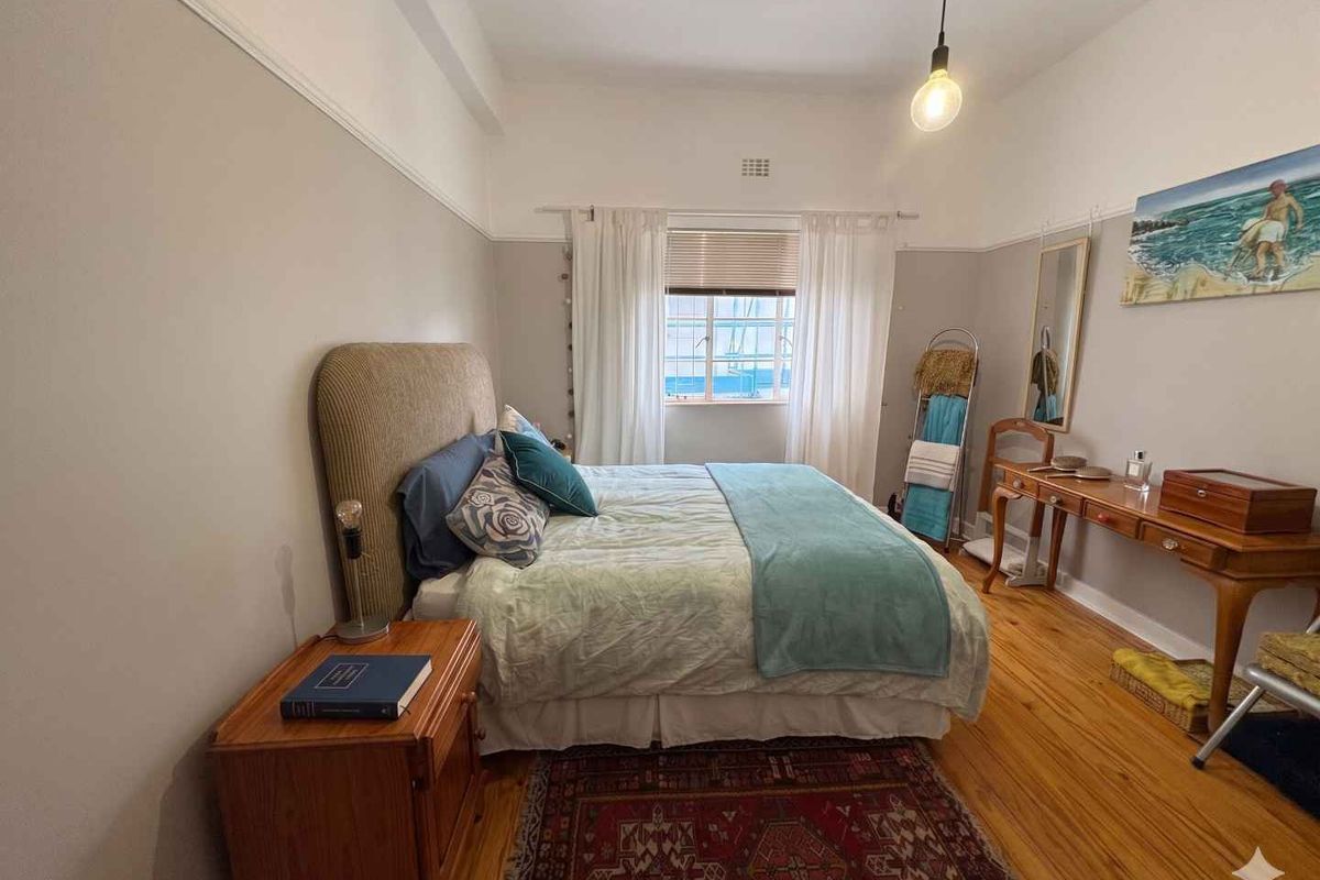 A well-proportioned bedroom featuring polished timber flooring, high ceilings with picture rails, and a large window providing natural light.