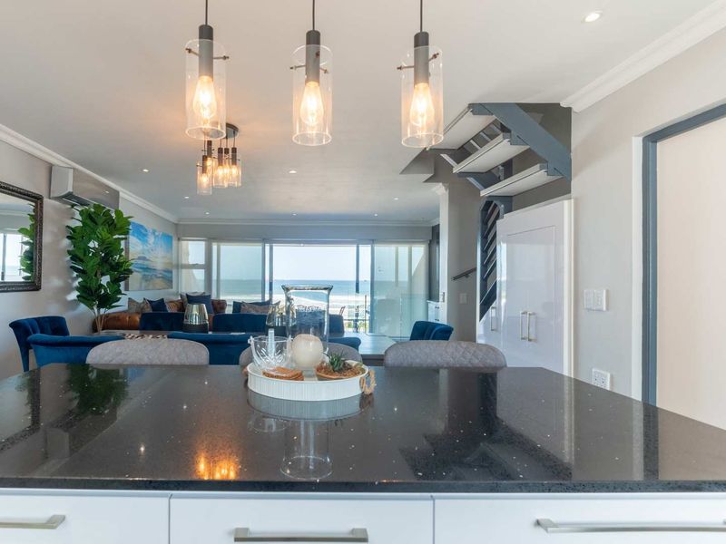 Open plan living area featuring a modern kitchen with granite countertops, pendant lighting, and seamless flow to a balcony with ocean views.