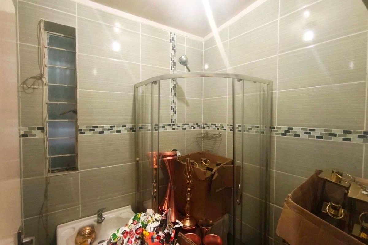 A bathroom featuring a corner shower enclosure and tiled walls with a decorative mosaic border.