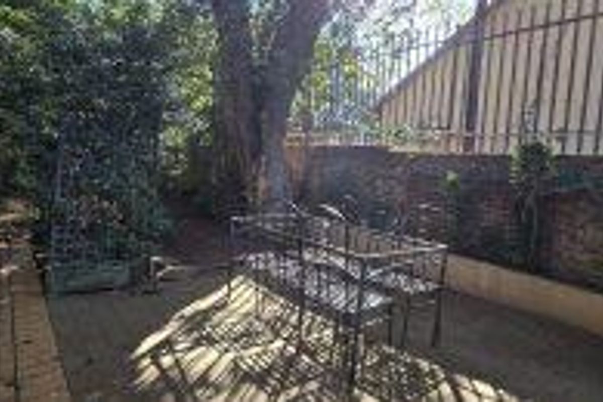 A private rear courtyard area featuring brick paving, a mature tree, and secure boundary walls with metal fencing.