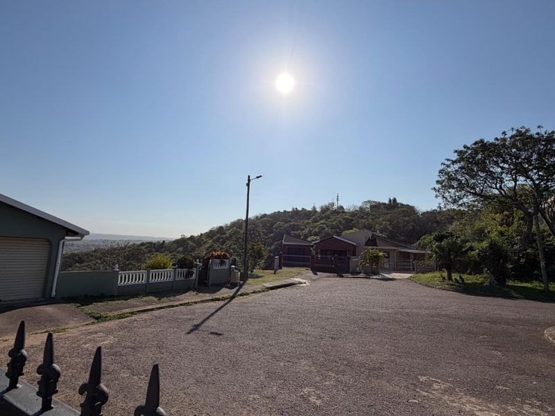Street view of the townhouse property featuring a paved driveway, garage, and surrounding perimeter fencing with elevated hillside views.