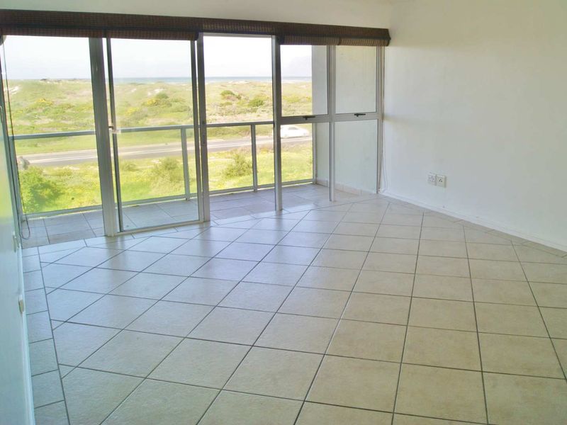 An empty, tiled living area featuring large sliding glass doors that provide access to a balcony and offer scenic coastal views.