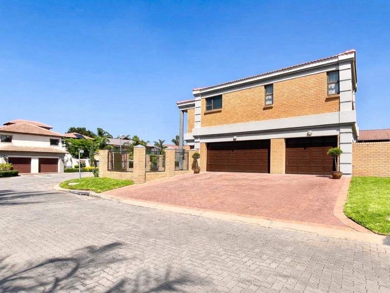 Front exterior view of a double-story cluster home featuring a double garage, paved driveway, and facebrick facade within a residential estate.