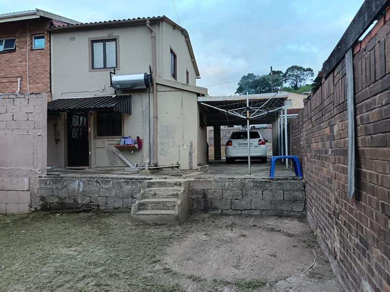 Rear view of the property featuring a carport, solar water heater, and a tiered backyard with brick boundary walls and concrete stairs.