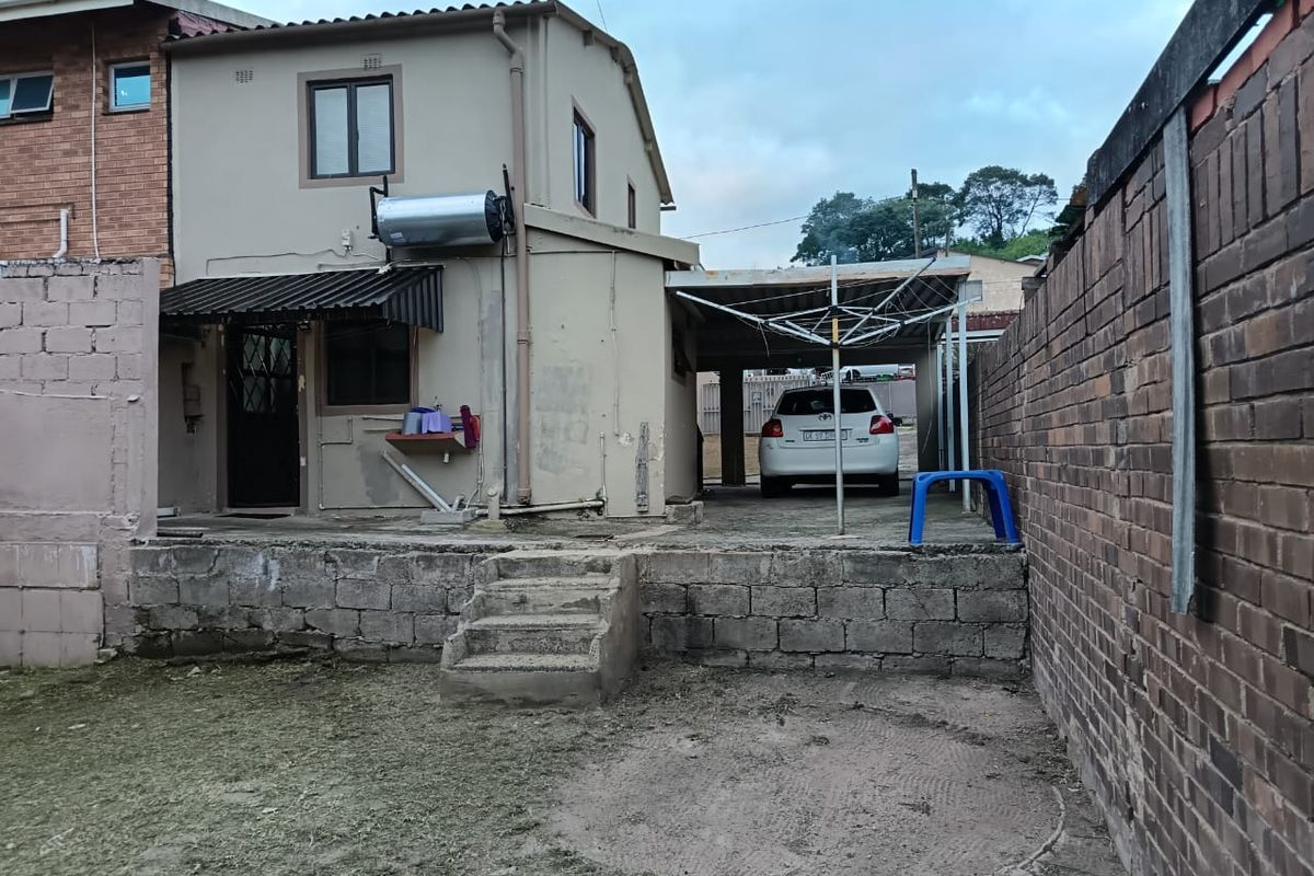 Rear view of the property featuring a carport, solar water heater, and a tiered backyard with brick boundary walls and concrete stairs.