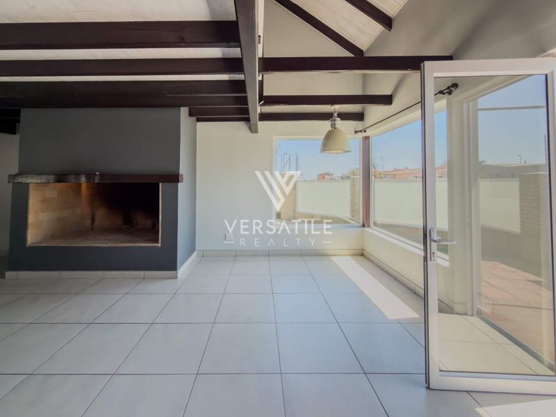 Spacious living area featuring exposed timber ceiling beams, a built-in fireplace, tiled flooring, and large glass doors opening to the exterior.