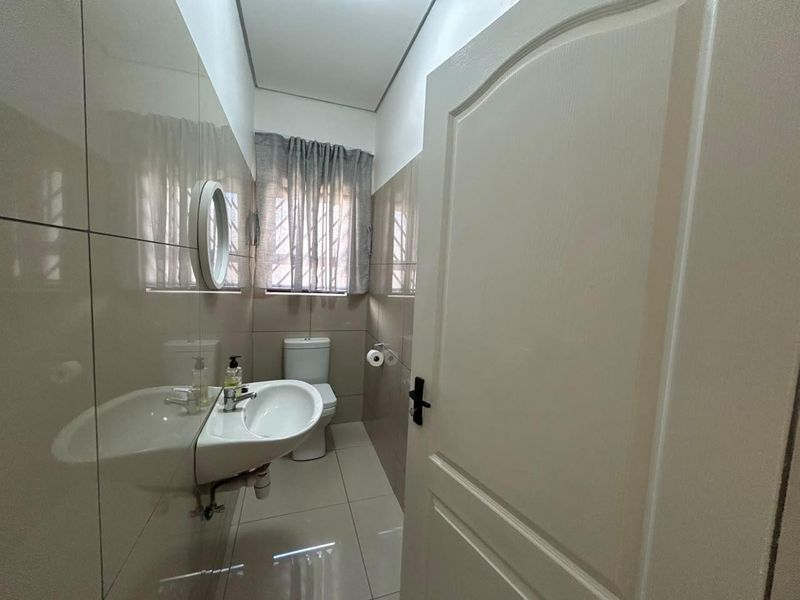 A compact, modern bathroom featuring neutral wall and floor tiles, a wall-mounted basin, and a toilet.