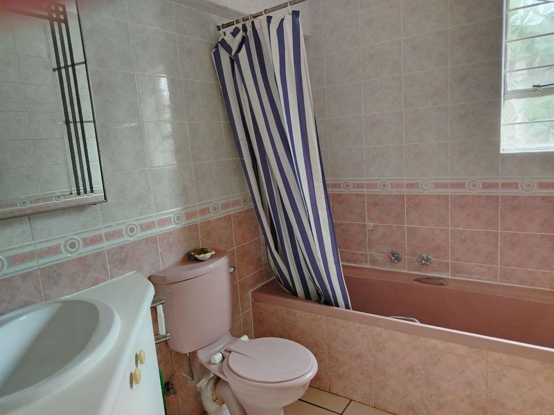 A dated bathroom featuring a pink bathtub and toilet suite with matching wall tiles and a vanity basin.