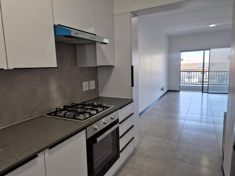 Modern open-plan kitchen featuring sleek white cabinetry, stone countertops, and integrated gas hob, flowing into a bright living area with balcony access.