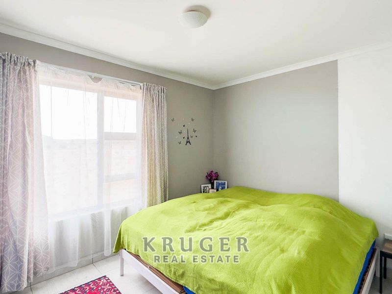 A well-lit bedroom featuring neutral wall tones, tiled flooring, and a large window with curtain fixtures.