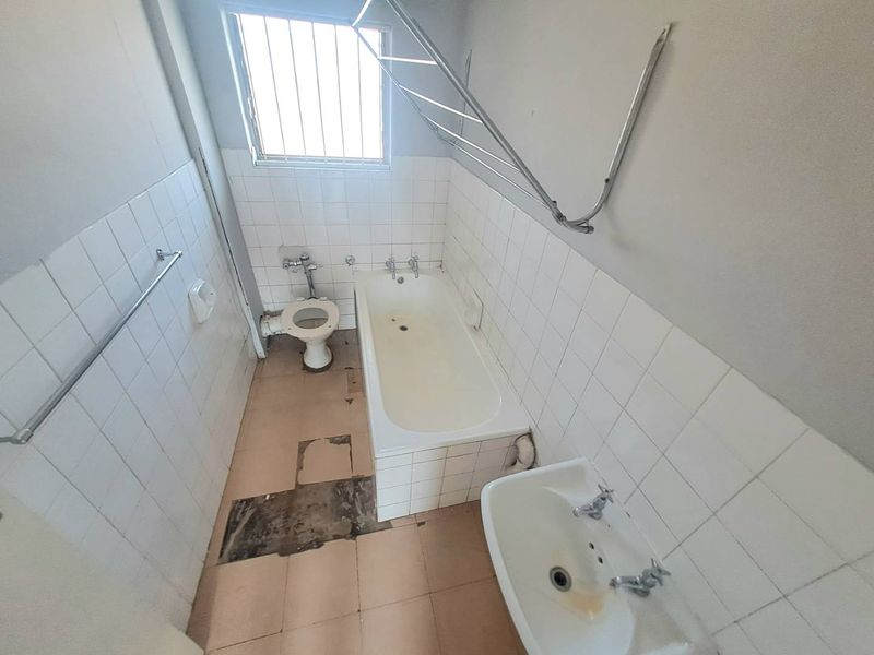 A dated bathroom featuring a bathtub, toilet, and pedestal basin, requiring significant renovation and floor tile repairs to modernize the space.