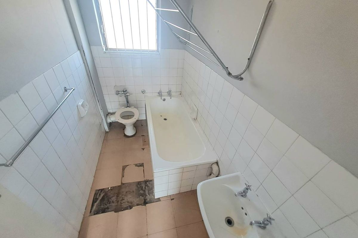 A dated bathroom featuring a bathtub, toilet, and pedestal basin, requiring significant renovation and floor tile repairs to modernize the space.