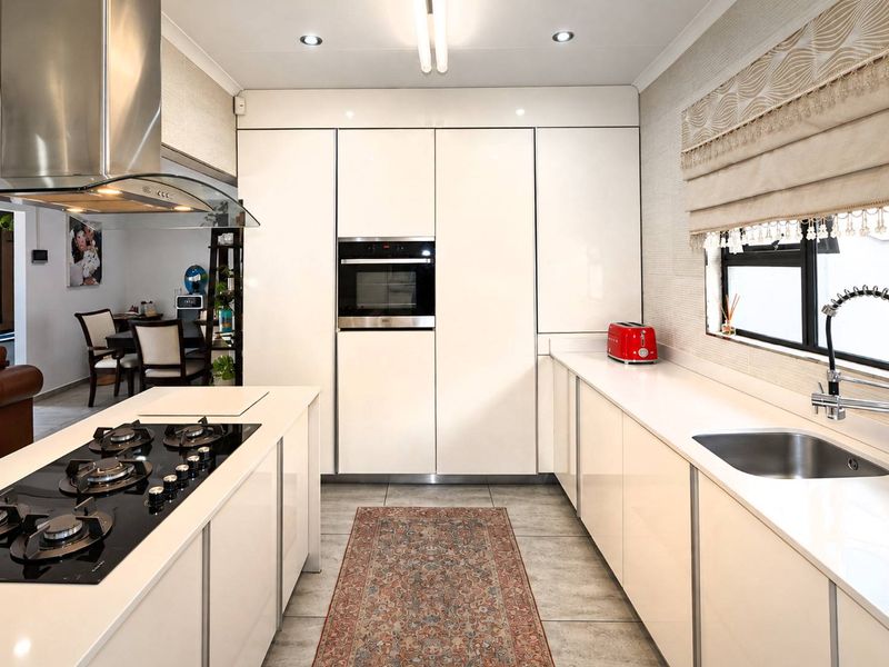 Modern kitchen featuring high-gloss cabinetry, stone countertops, a central island with a gas hob, and integrated appliances.