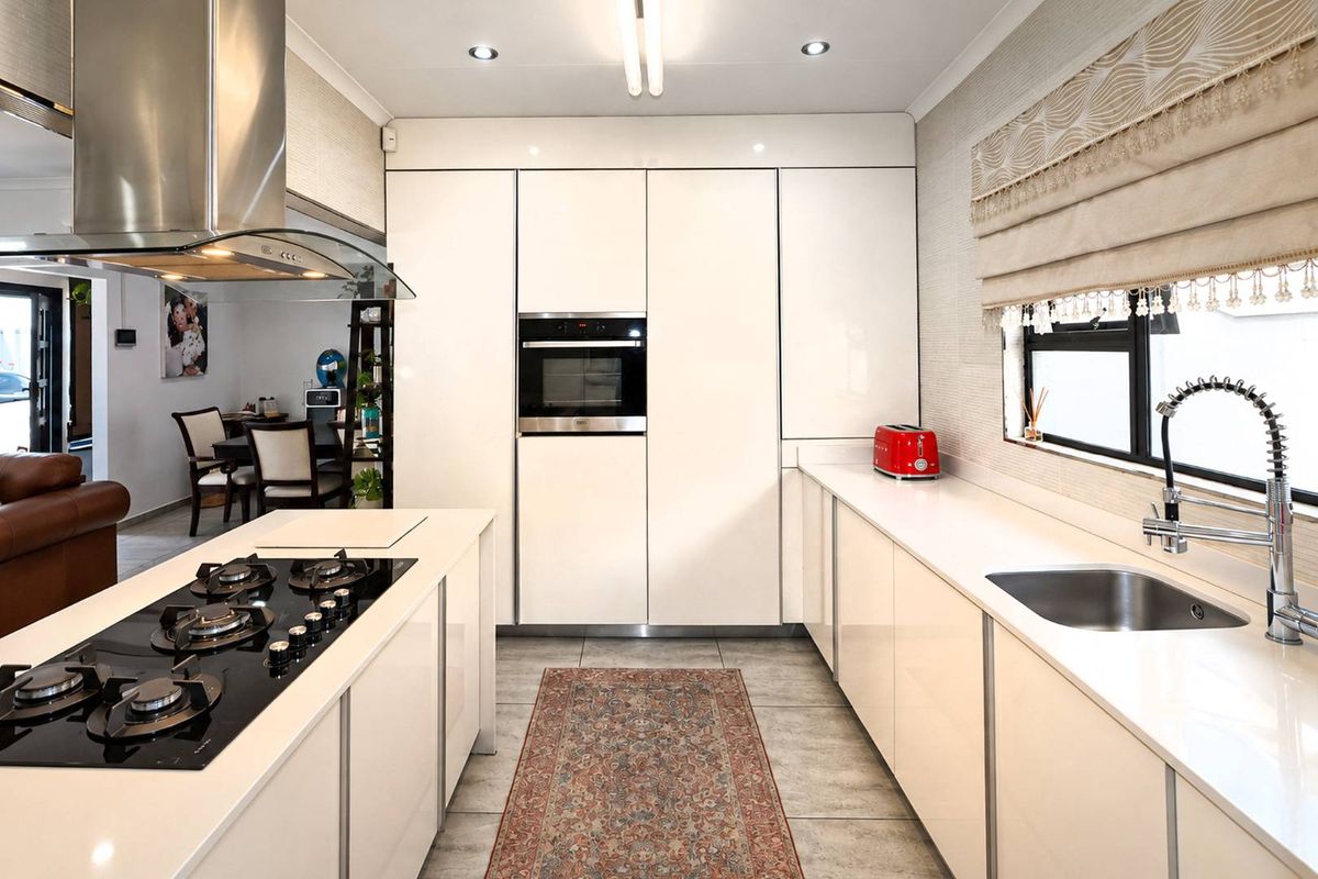 Modern kitchen featuring high-gloss cabinetry, stone countertops, a central island with a gas hob, and integrated appliances.