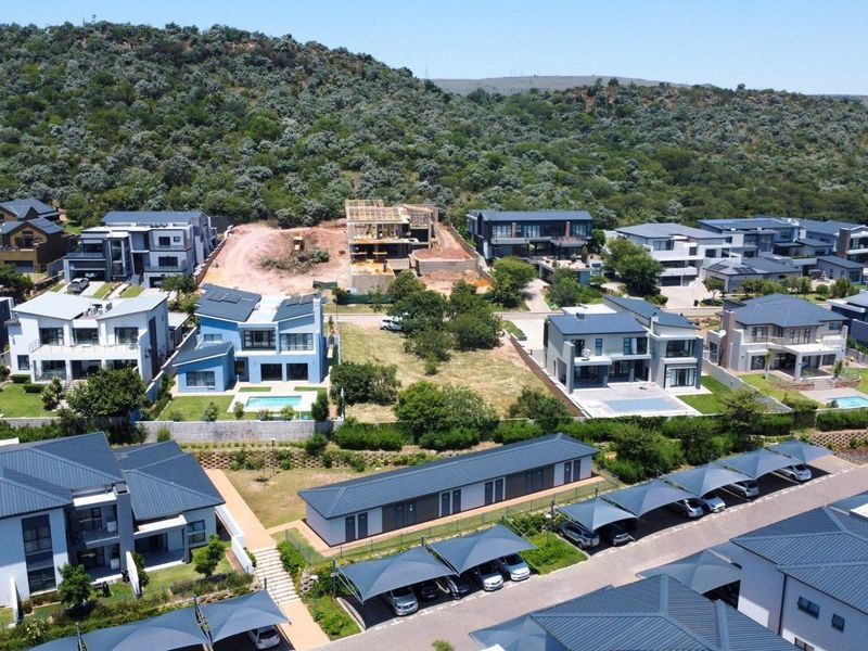 Aerial view of a residential estate featuring a vacant land plot surrounded by modern multi-story homes and communal parking facilities.