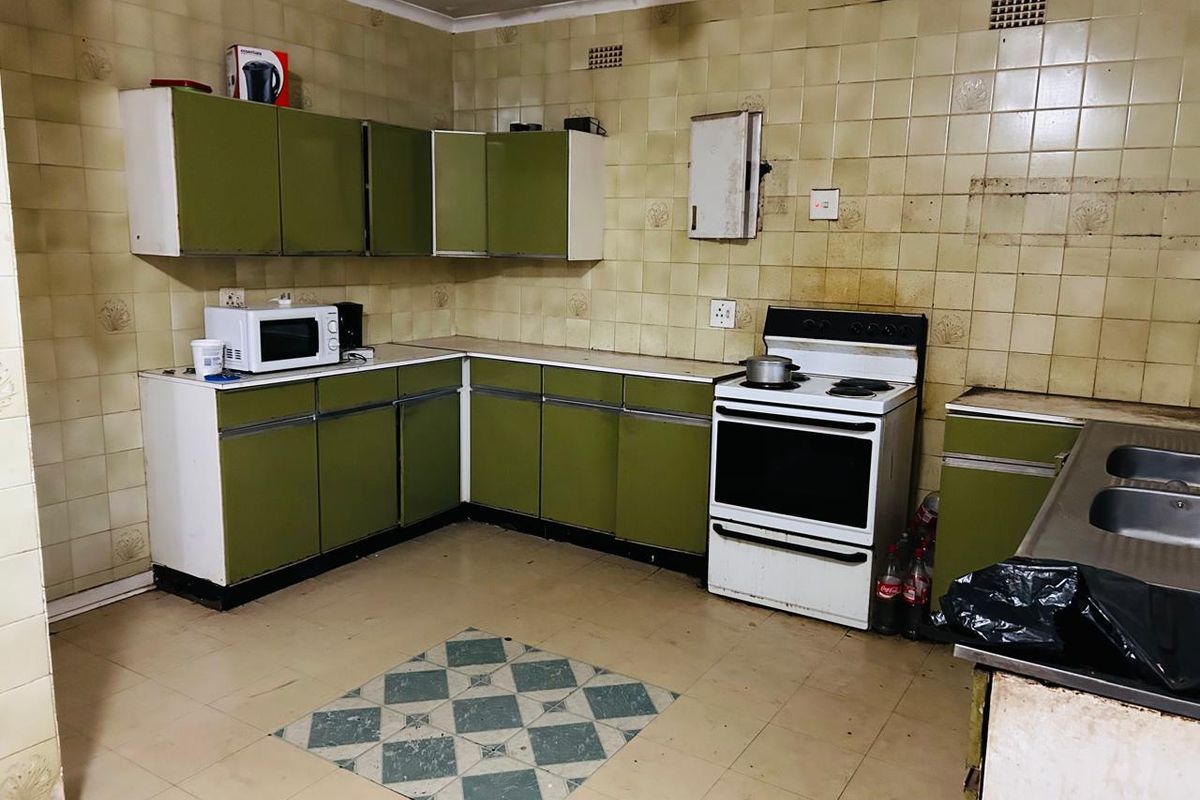 A dated kitchen featuring original cabinetry, tiled splashbacks, and a freestanding stove, requiring significant renovation and ceiling repairs to modernize the space.