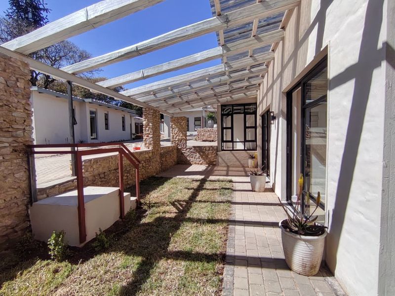 A covered outdoor patio area featuring a timber pergola, stone-clad pillars, and paved flooring, providing a seamless transition between indoor and outdoor living spaces.