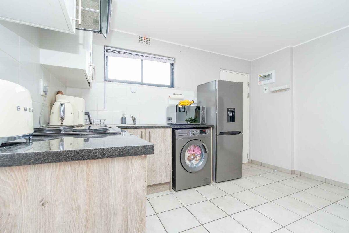 A functional kitchen featuring light wood-look cabinetry, dark granite countertops, tiled flooring, and integrated space for laundry appliances.
