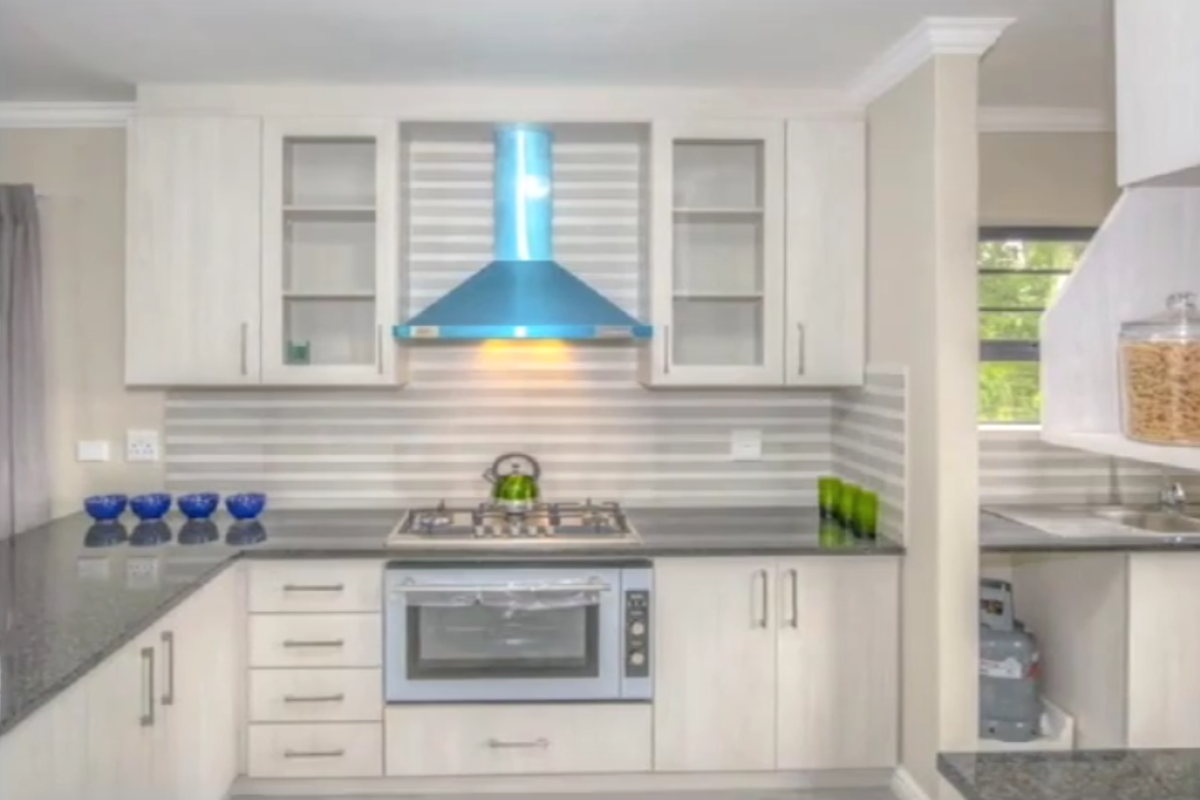 Modern kitchen featuring light wood cabinetry, granite countertops, a built-in gas hob, and a stainless steel oven with a prominent blue extractor hood.