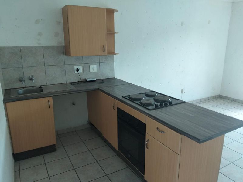 Compact kitchen featuring laminate cabinetry, built-in oven and hob, and tiled finishes. The space is vacant and requires cosmetic wall repairs.