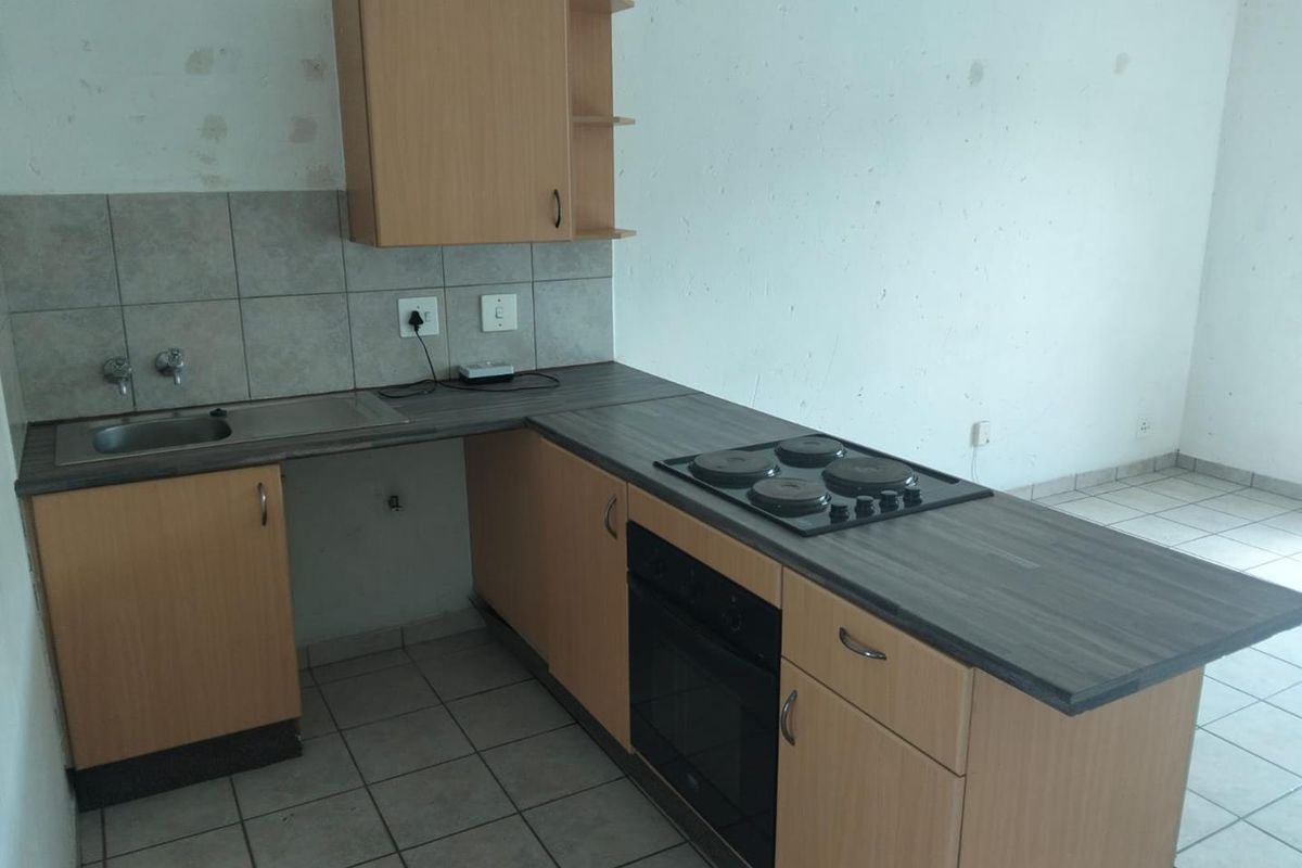 Compact kitchen featuring laminate cabinetry, built-in oven and hob, and tiled finishes. The space is vacant and requires cosmetic wall repairs.