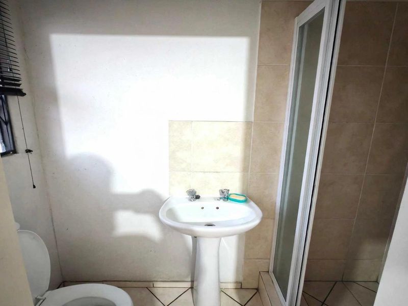 A functional bathroom featuring a pedestal basin, a shower enclosure, and tiled finishes, presenting a clean and basic layout.