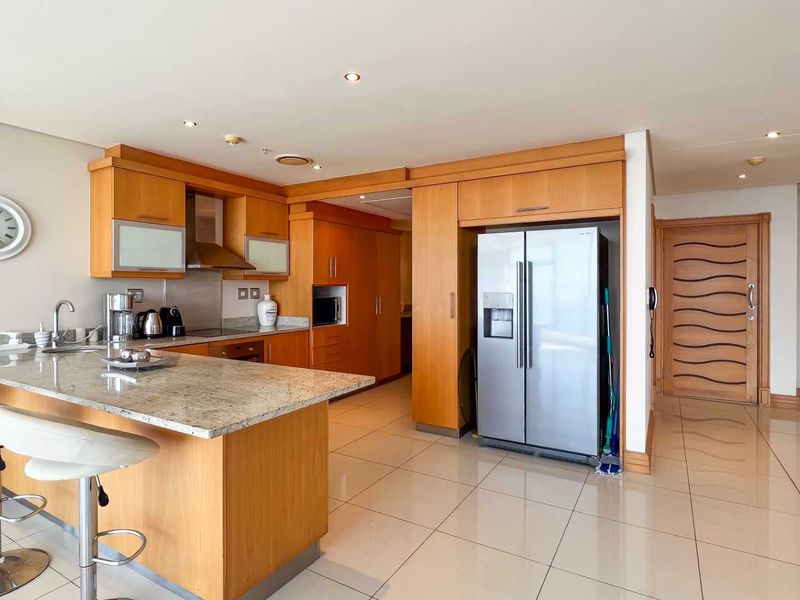A functional kitchen featuring light wood cabinetry, granite countertops, a breakfast bar, and integrated appliances, set within an open-plan living space.