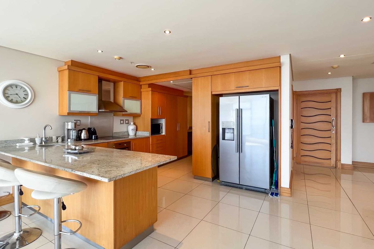A functional kitchen featuring light wood cabinetry, granite countertops, a breakfast bar, and integrated appliances, set within an open-plan living space.
