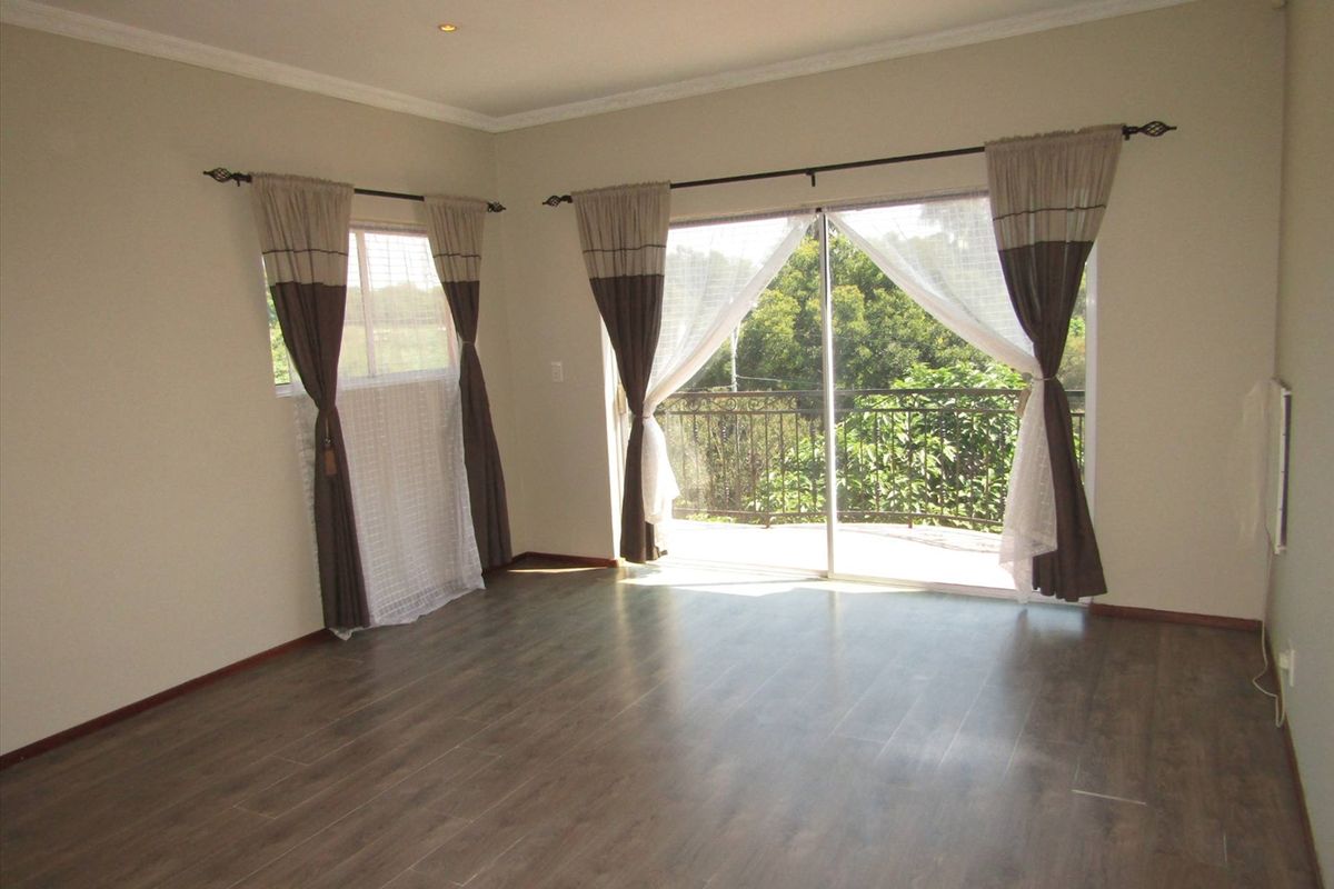 Spacious living room featuring wood-look laminate flooring, recessed ceiling lighting, and sliding glass doors opening onto a balcony with scenic views.