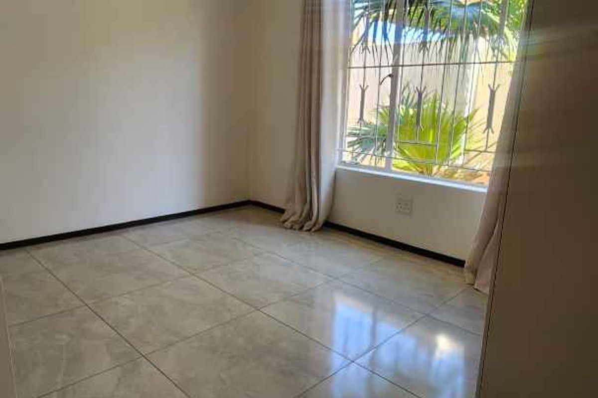 A bright, empty bedroom featuring neutral floor tiles, a built-in wardrobe, and security bars on the window.