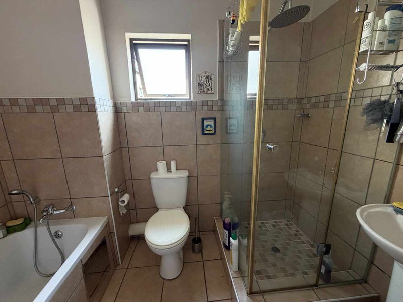 A functional bathroom featuring a shower enclosure, bathtub, pedestal basin, and tiled finishes throughout.