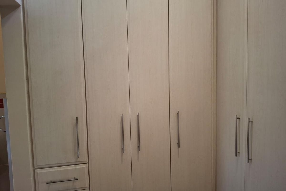 A bedroom featuring light-toned built-in cupboards with modern metal handles, providing ample integrated storage space.