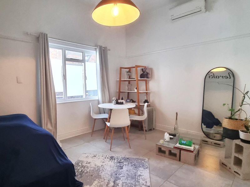 A bright living area featuring tiled flooring, a wall-mounted air conditioning unit, and a classic picture rail detail.