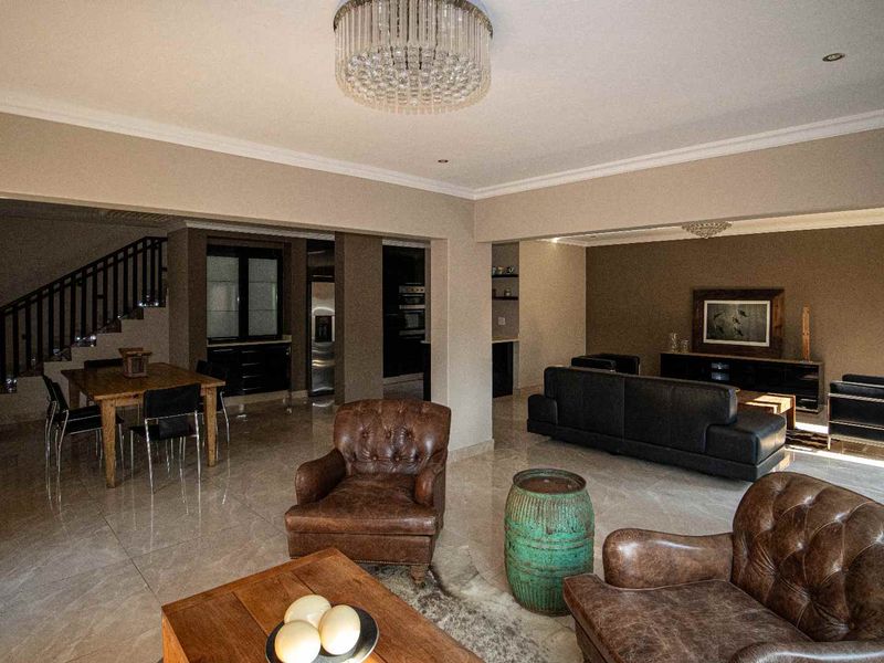 Spacious open-plan living and dining area featuring polished tiled floors, elegant crystal chandeliers, and a staircase with a wooden balustrade.