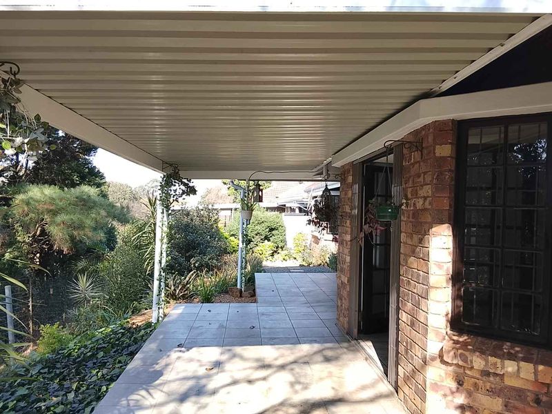 A covered patio area featuring tiled flooring and a corrugated metal roof, providing direct access to the garden through a sliding door.