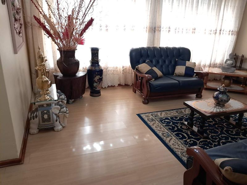 A living room featuring light-toned laminate flooring and a large window with sheer curtains, providing a bright and neutral foundation for the space.