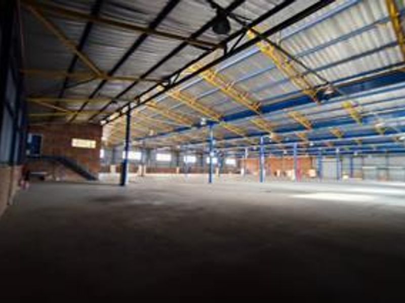 Expansive industrial warehouse space featuring high ceilings with exposed steel trusses, concrete flooring, and robust steel support columns.