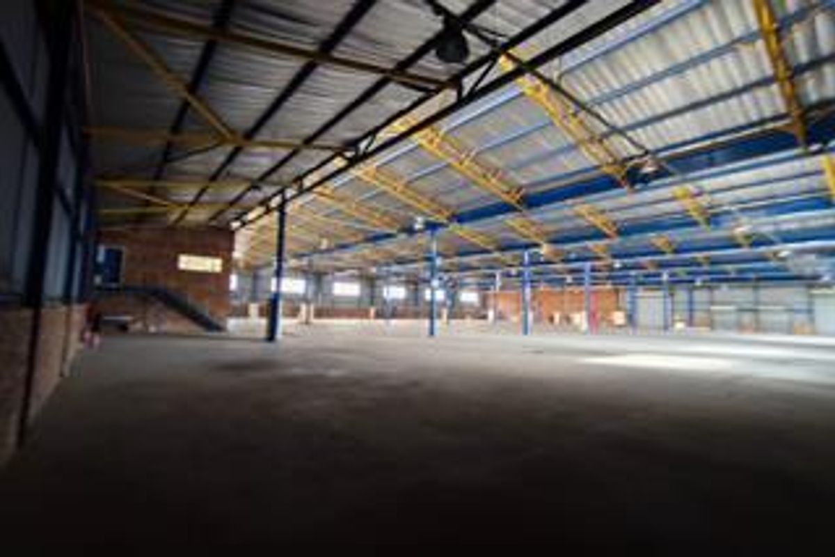 Expansive industrial warehouse space featuring high ceilings with exposed steel trusses, concrete flooring, and robust steel support columns.