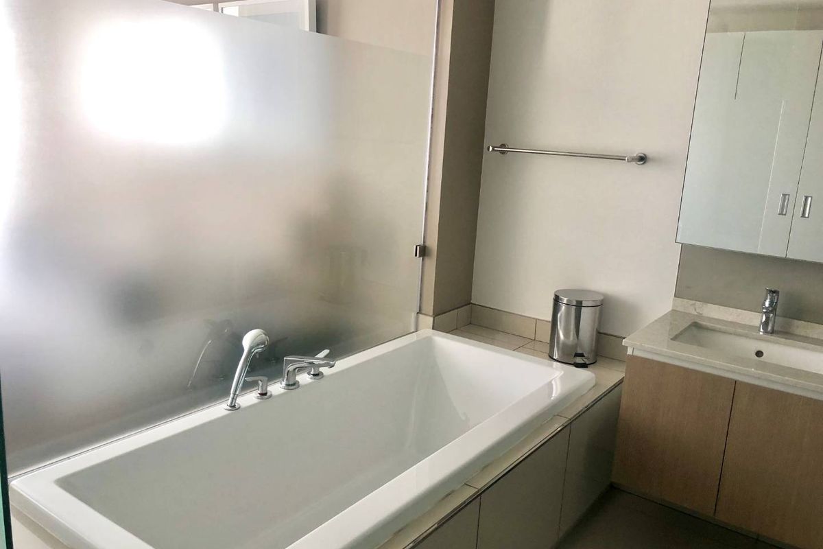 Modern bathroom featuring a built-in bathtub with a frosted glass screen, a vanity with stone countertop, and a wall-mounted mirror cabinet.