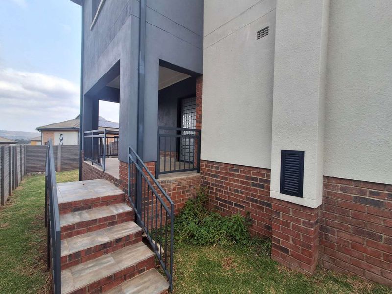 A well-maintained rear exterior view featuring a tiled staircase with metal balustrades leading to a covered patio area with brick and plaster finishes.