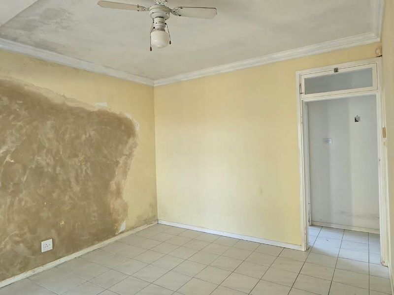 An empty bedroom featuring tiled flooring, a ceiling fan, and cornicing, currently requiring wall repairs and cosmetic updates to restore its condition.