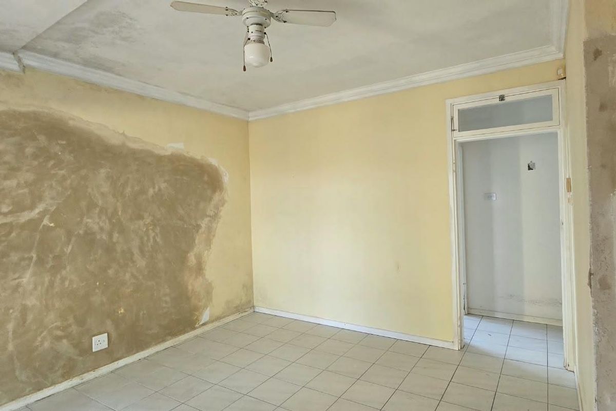 An empty bedroom featuring tiled flooring, a ceiling fan, and cornicing, currently requiring wall repairs and cosmetic updates to restore its condition.