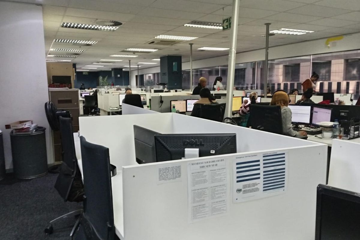 A large open-plan office space featuring suspended ceilings, recessed lighting, carpeted floors, and multiple built-in workstation partitions with large windows.